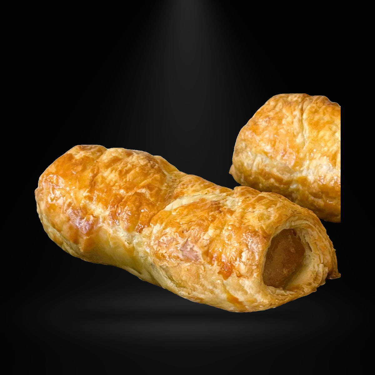 Jolly Posh Traditional Sausage Rolls 3Pack on a black background with an overhead spotlight
